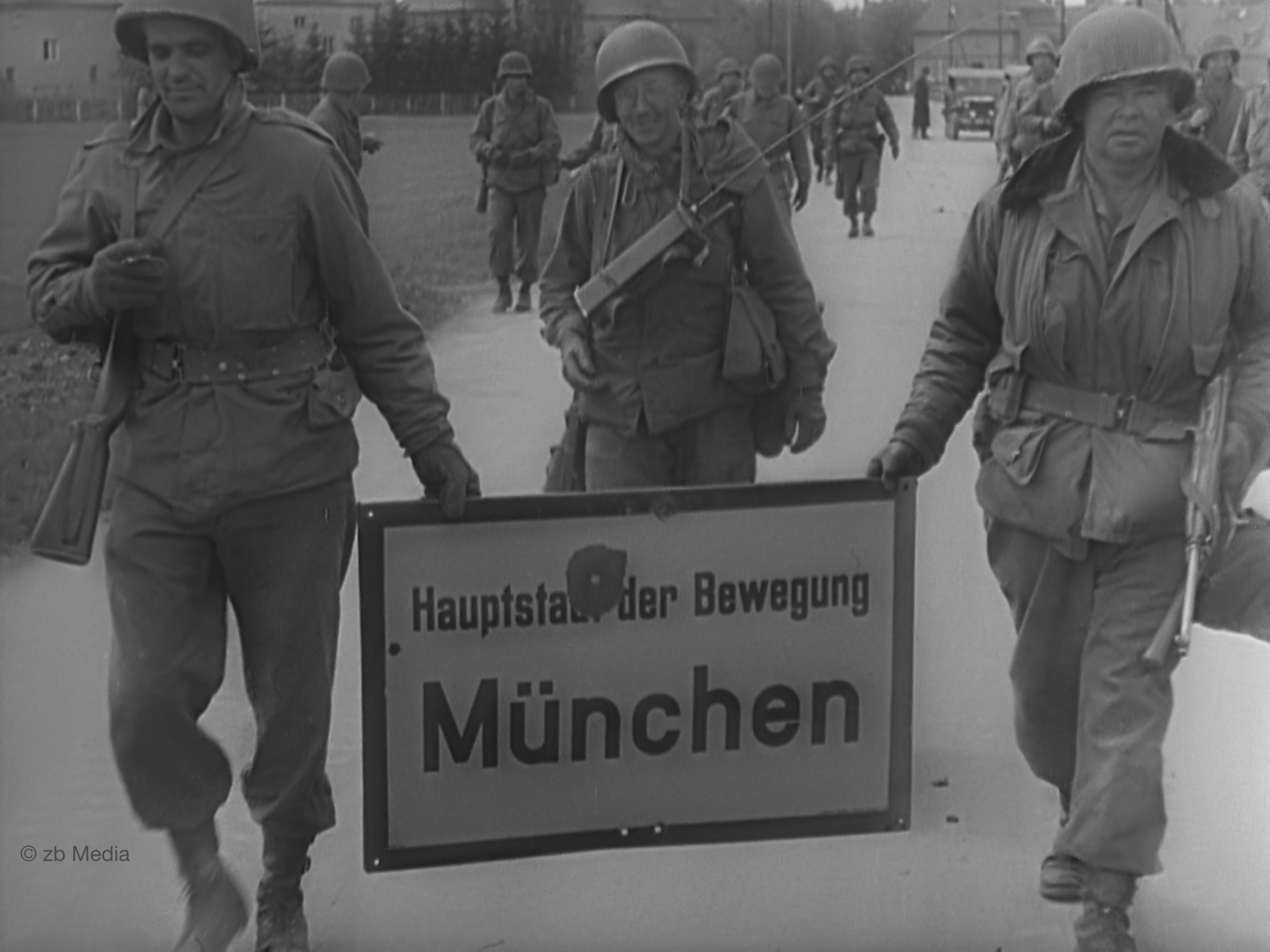 Amerikanische Soldaten am 30. April 1945 mit dem Ortsschild Hauptstadt der Bewegung München.