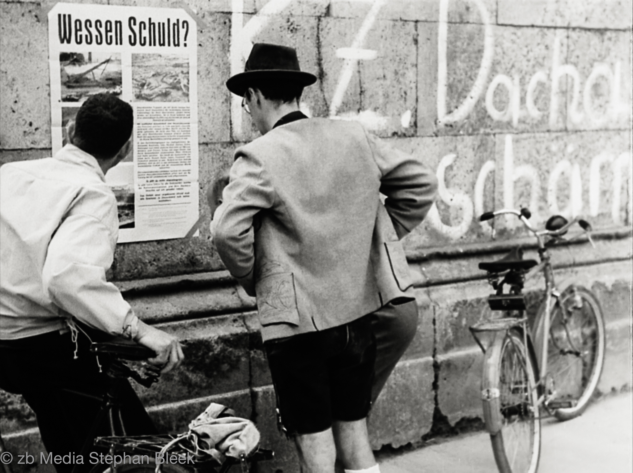 Münchner Bürger lesen Plakat "Wessen Schuld?"